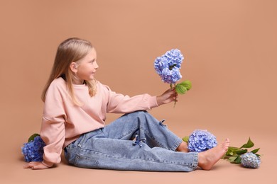 Photo of Smiling little girl with hortensia flowers on beige background