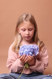 Photo of Beautiful little girl with hortensia flowers on beige background