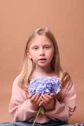 Photo of Portrait of beautiful little girl with hortensia flowers on beige background