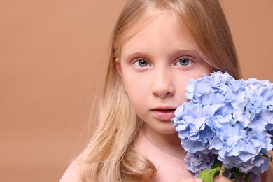 Photo of Portrait of beautiful little girl with hortensia flowers on beige background, closeup. Space for text