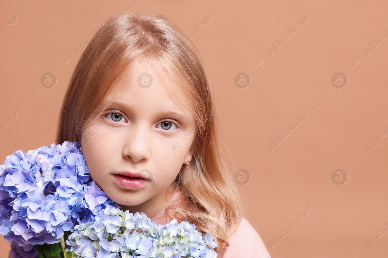 Portrait of beautiful little girl with hortensia flowers on beige background, closeup. Space for text Photo of Portrait of beautiful little girl with hortensia flowers on beige background, closeup. Space for text