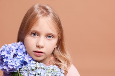 Photo of Portrait of beautiful little girl with hortensia flowers on beige background, closeup. Space for text