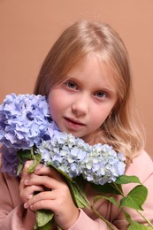 Photo of Portrait of beautiful little girl with hortensia flowers on beige background, closeup
