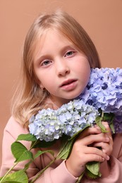 Photo of Portrait of beautiful little girl with hortensia flowers on beige background, closeup