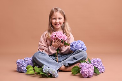 Photo of Smiling little girl with hortensia flowers on beige background