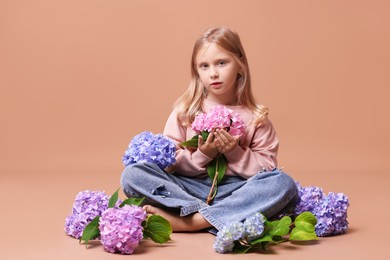 Photo of Beautiful little girl with hortensia flowers on beige background