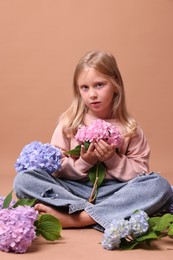 Photo of Beautiful little girl with hortensia flowers on beige background