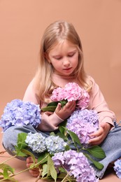 Photo of Beautiful little girl with hortensia flowers on beige background