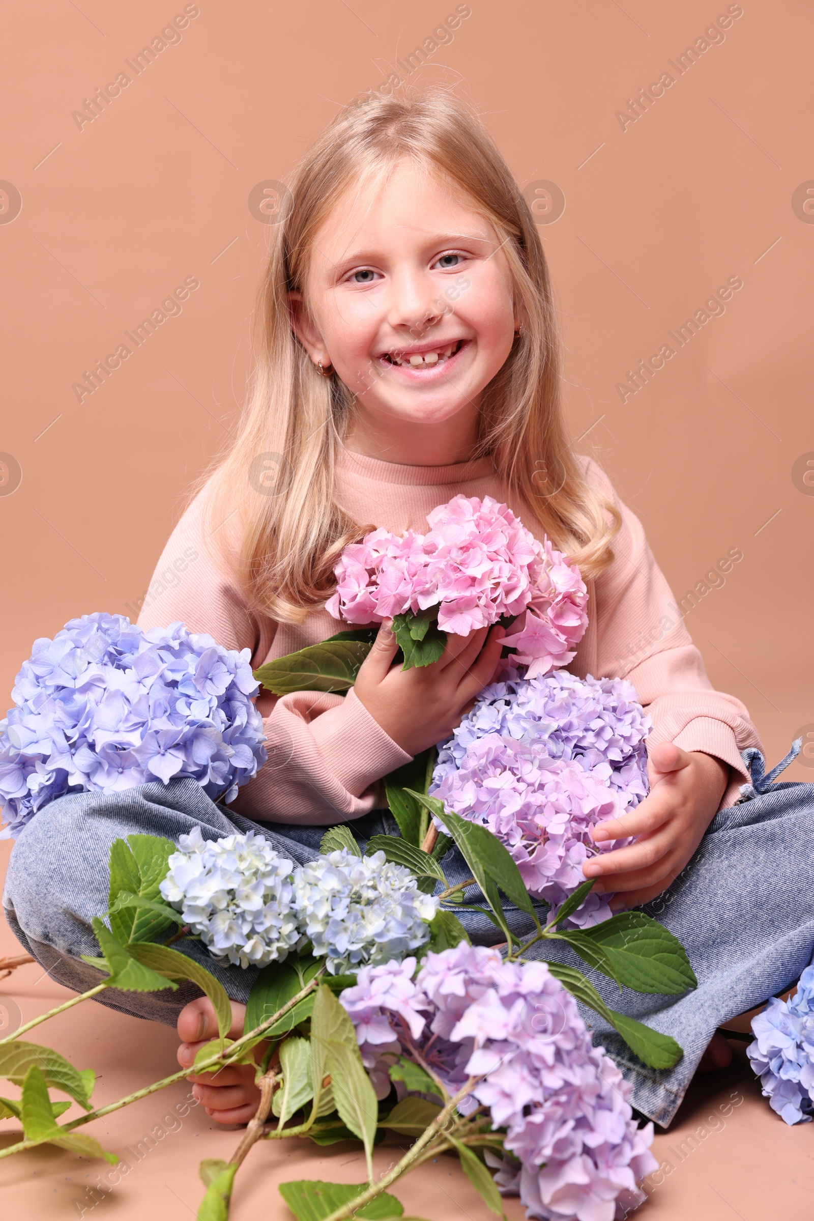 Photo of Smiling little girl with hortensia flowers on beige background