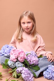 Photo of Beautiful little girl with hortensia flowers on beige background