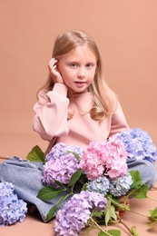 Photo of Beautiful little girl with hortensia flowers on beige background