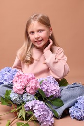 Photo of Smiling little girl with hortensia flowers on beige background