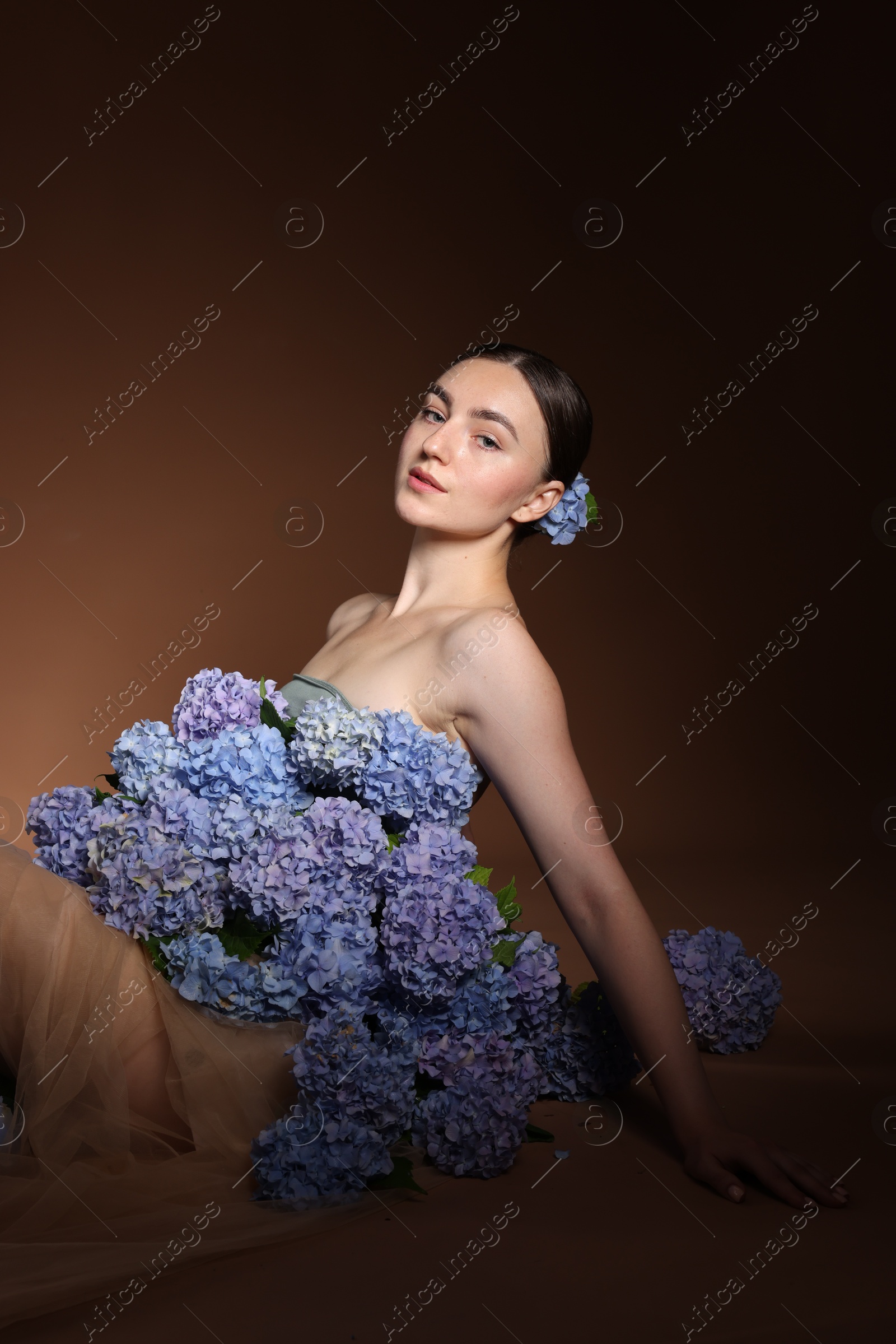 Photo of Beautiful young woman with hortensia flowers on brown background