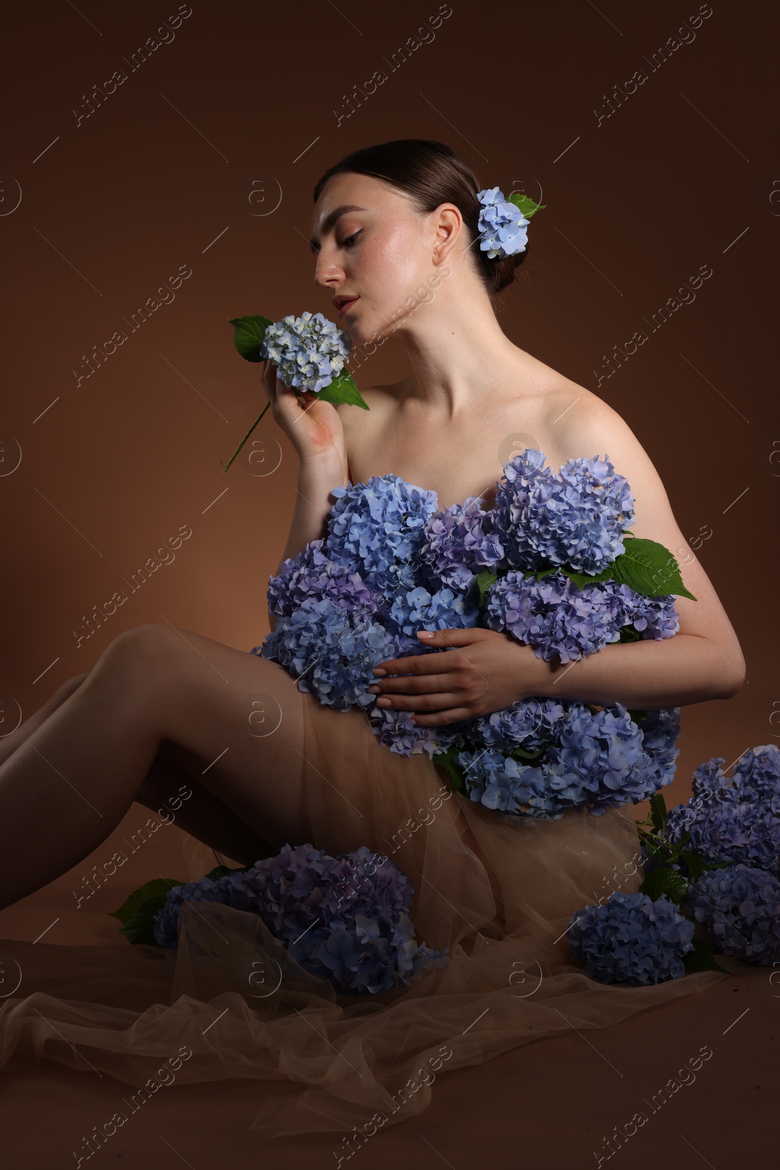 Photo of Beautiful young woman with hortensia flowers on brown background