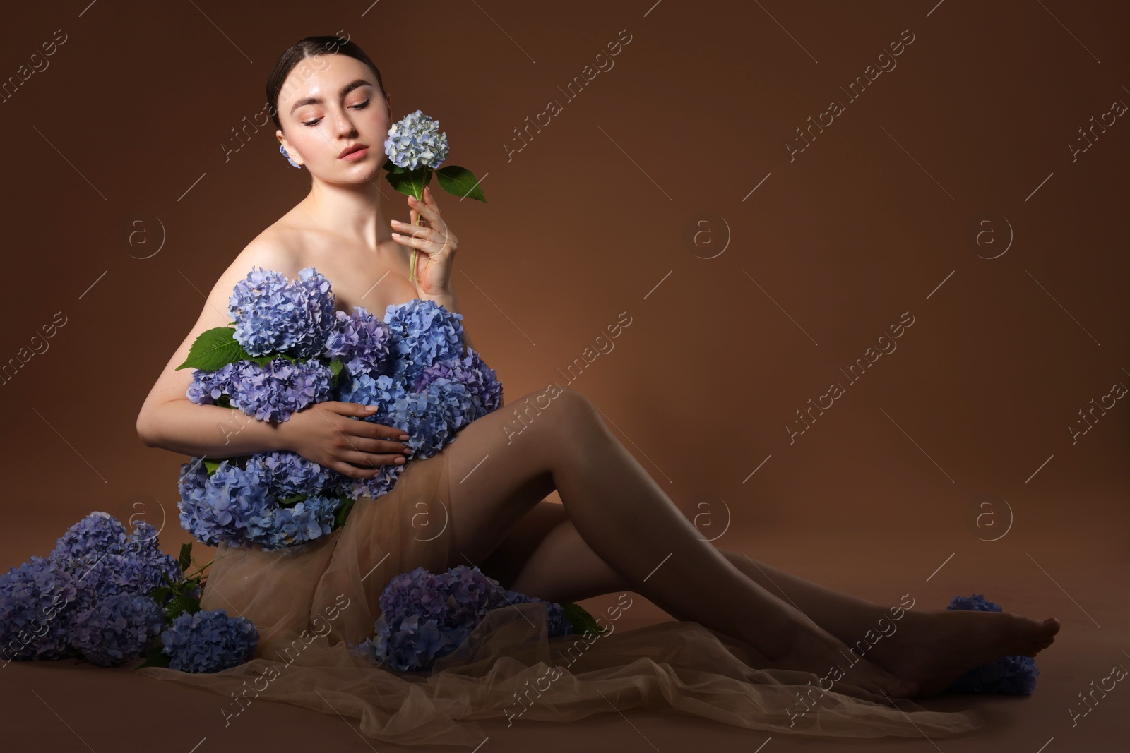 Beautiful young woman with hortensia flowers on brown background Photo of Beautiful young woman with hortensia flowers on brown background