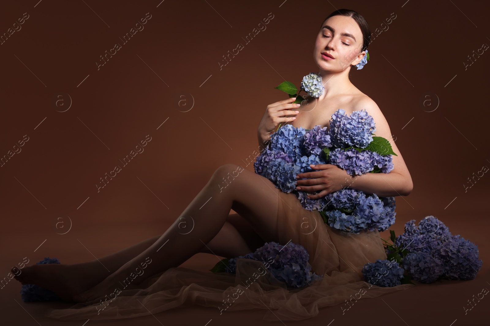 Beautiful young woman with hortensia flowers on brown background Photo of Beautiful young woman with hortensia flowers on brown background