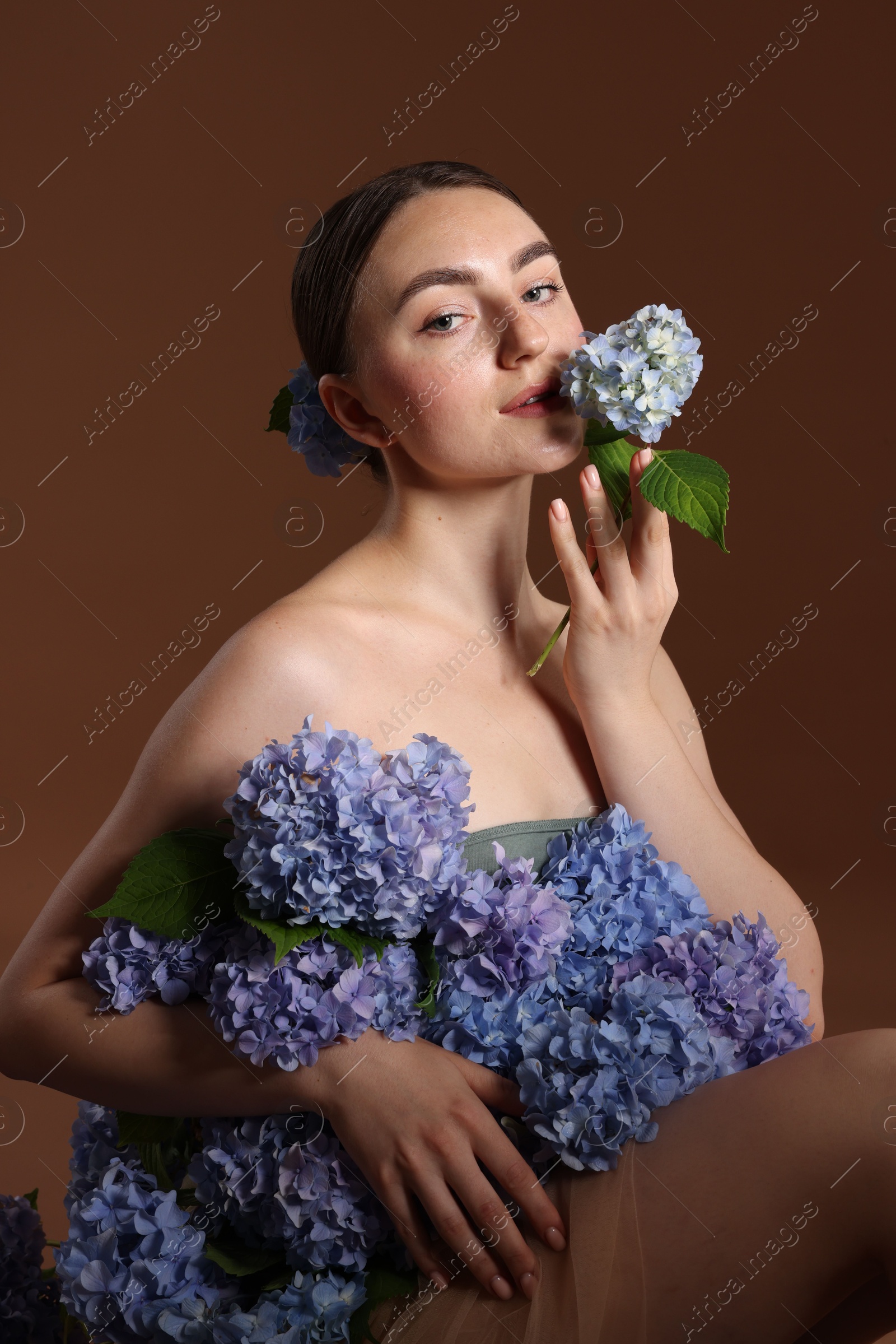 Photo of Beautiful young woman with hortensia flowers on brown background