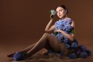 Photo of Beautiful young woman with hortensia flowers on brown background