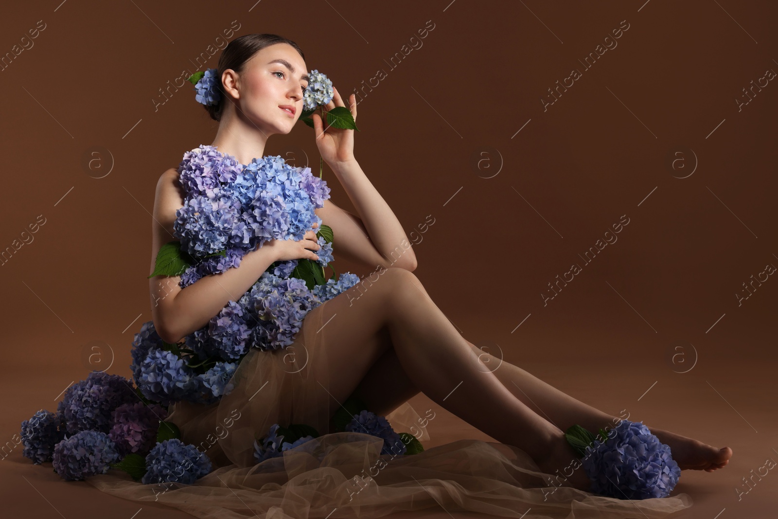 Photo of Beautiful young woman with hortensia flowers on brown background