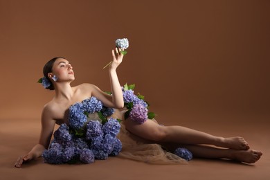 Photo of Beautiful young woman with hortensia flowers on brown background. Space for text