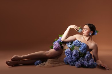 Photo of Beautiful young woman with hortensia flowers on brown background. Space for text