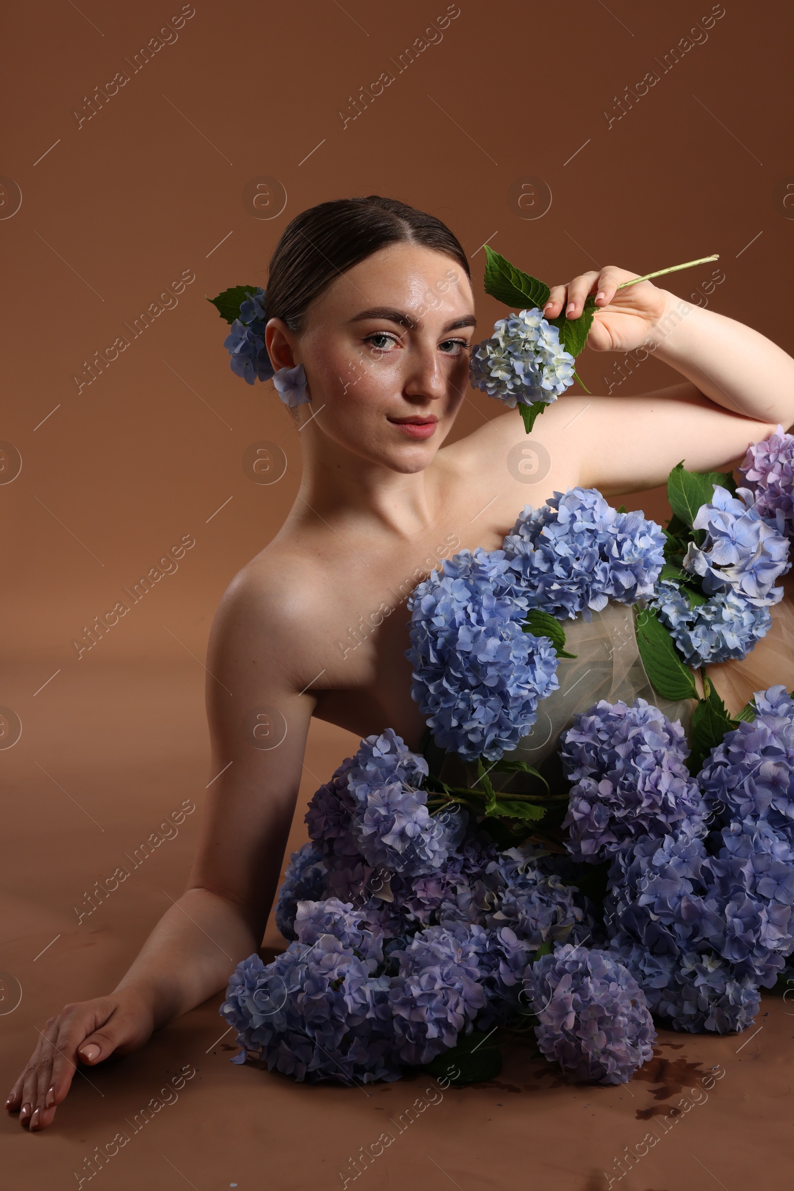 Photo of Beautiful young woman with hortensia flowers on brown background