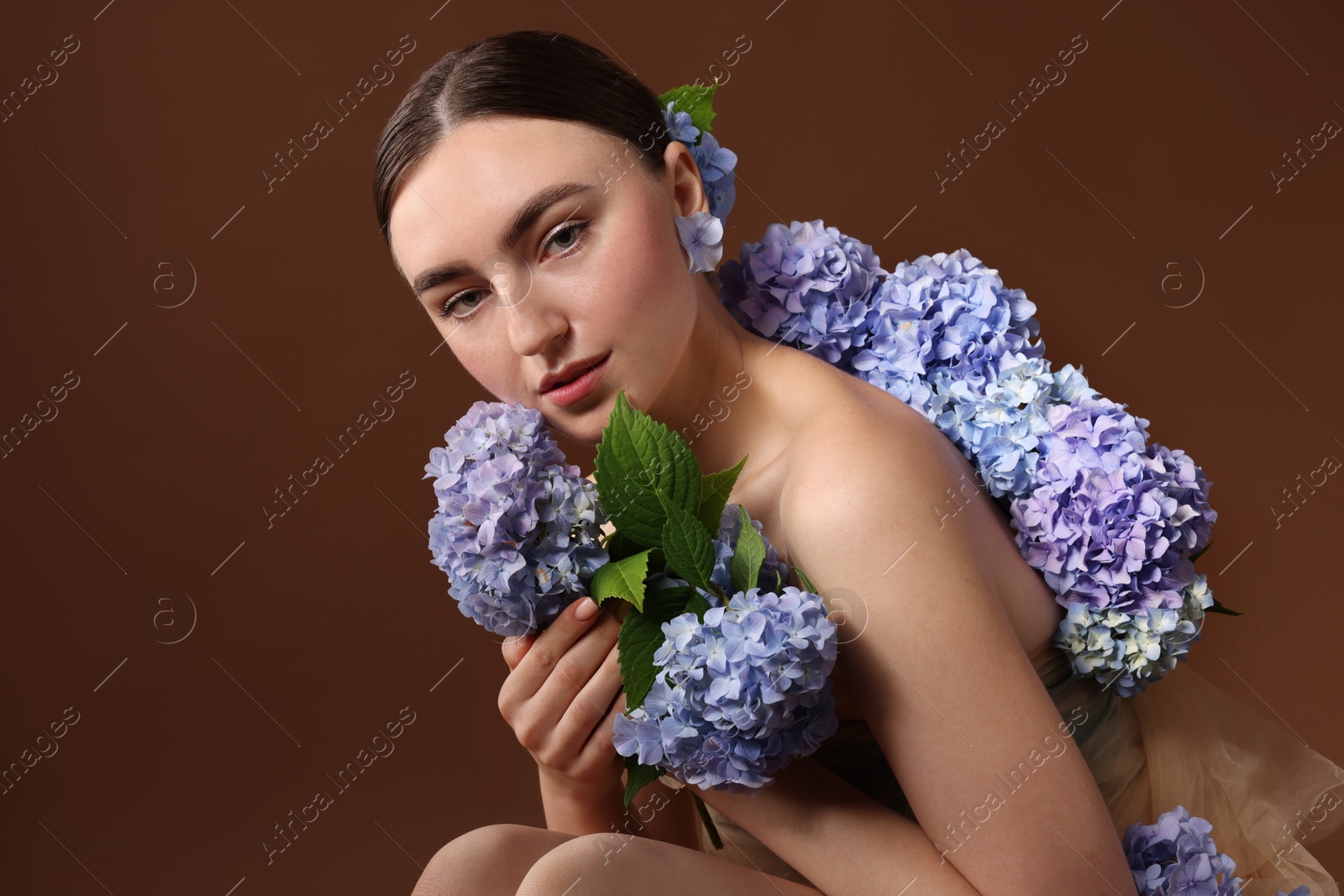 Photo of Beautiful young woman with hortensia flowers on brown background
