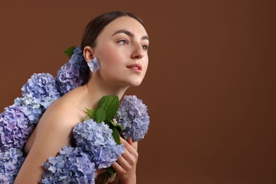 Photo of Beautiful young woman with hortensia flowers on brown background. Space for text