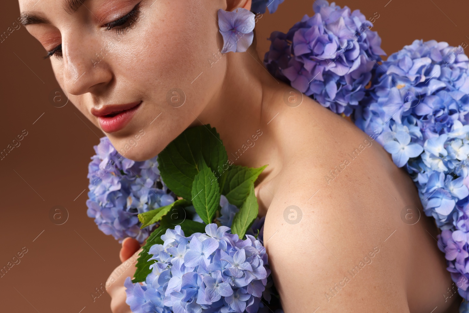 Photo of Beautiful young woman with hortensia flowers on brown background, closeup