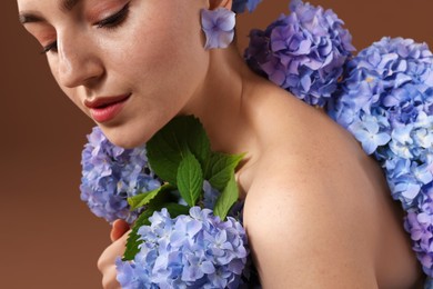 Photo of Beautiful young woman with hortensia flowers on brown background, closeup