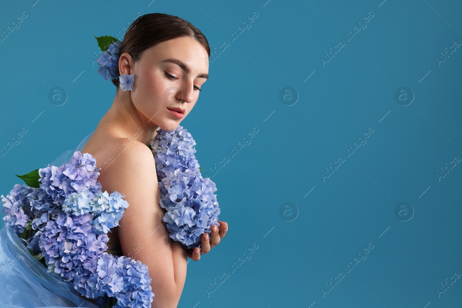 Portrait of beautiful woman with hortensia flowers on blue background. Space for text Photo of Portrait of beautiful woman with hortensia flowers on blue background. Space for text