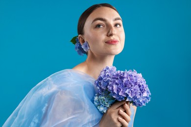 Photo of Portrait of beautiful woman with hortensia flowers and cloth on blue background