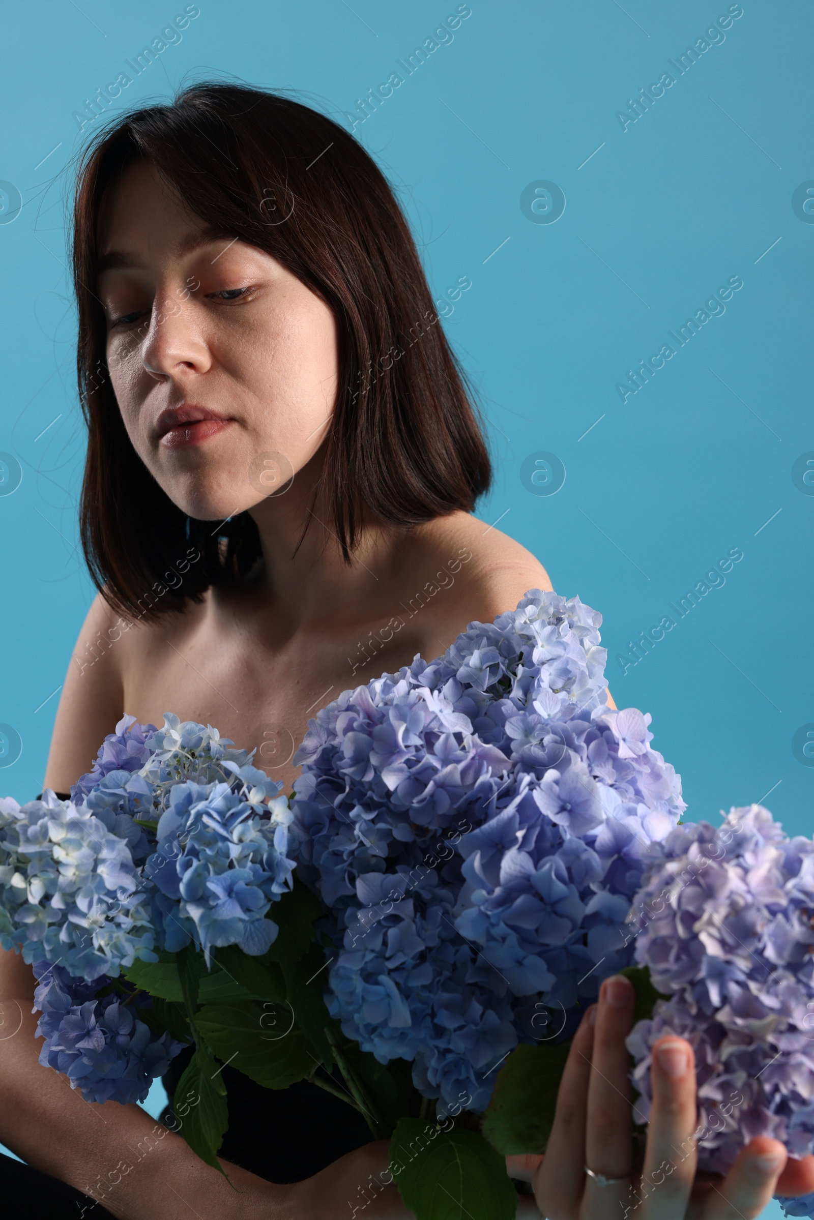 Photo of Beautiful young woman with hortensia flowers on light blue background