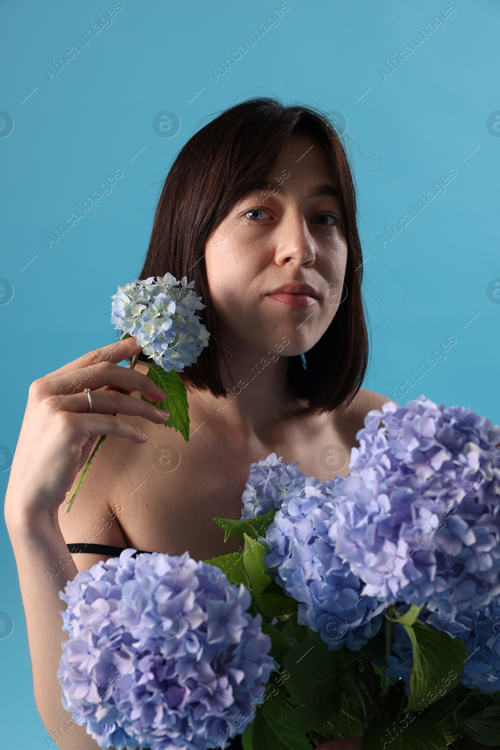 Photo of Beautiful young woman with hortensia flowers on light blue background