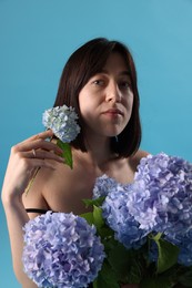 Photo of Beautiful young woman with hortensia flowers on light blue background