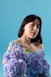 Photo of Beautiful young woman with hortensia flowers on light blue background