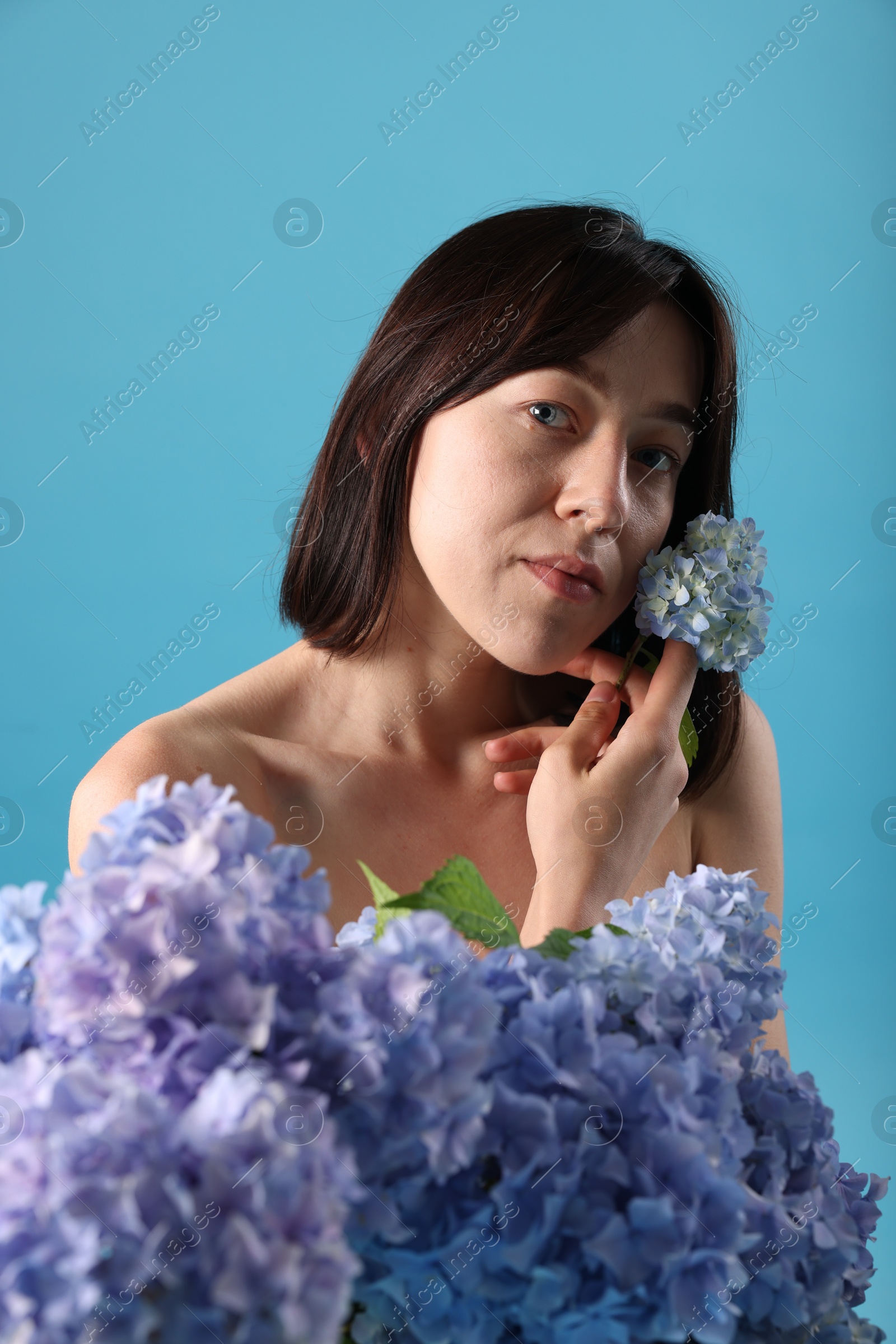 Photo of Beautiful young woman with hortensia flowers on light blue background