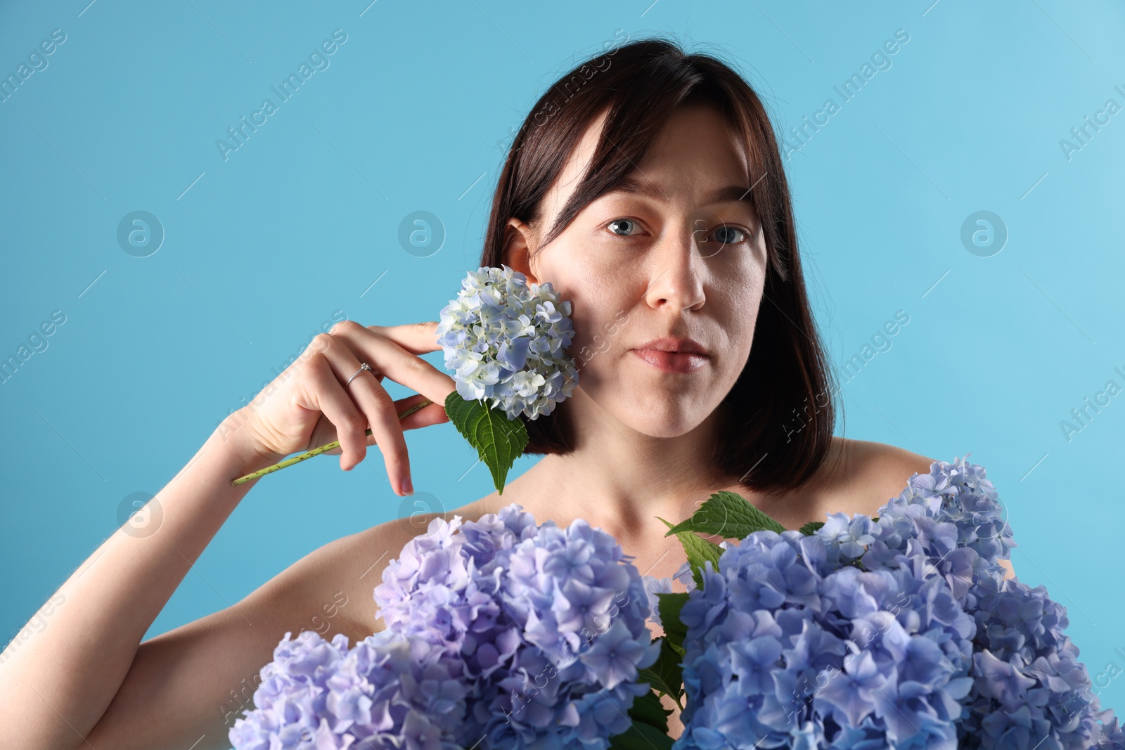 Photo of Beautiful young woman with hortensia flowers on light blue background