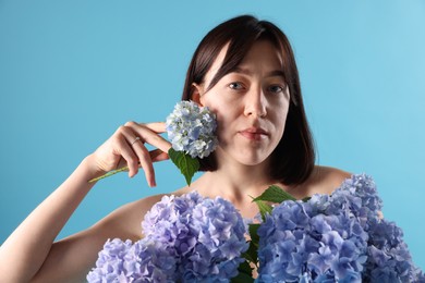 Photo of Beautiful young woman with hortensia flowers on light blue background
