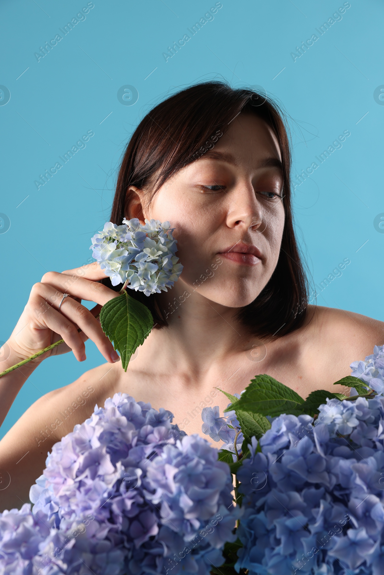 Photo of Beautiful young woman with hortensia flowers on light blue background