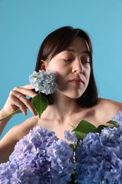 Photo of Beautiful young woman with hortensia flowers on light blue background