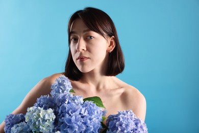 Photo of Beautiful young woman with hortensia flowers on light blue background