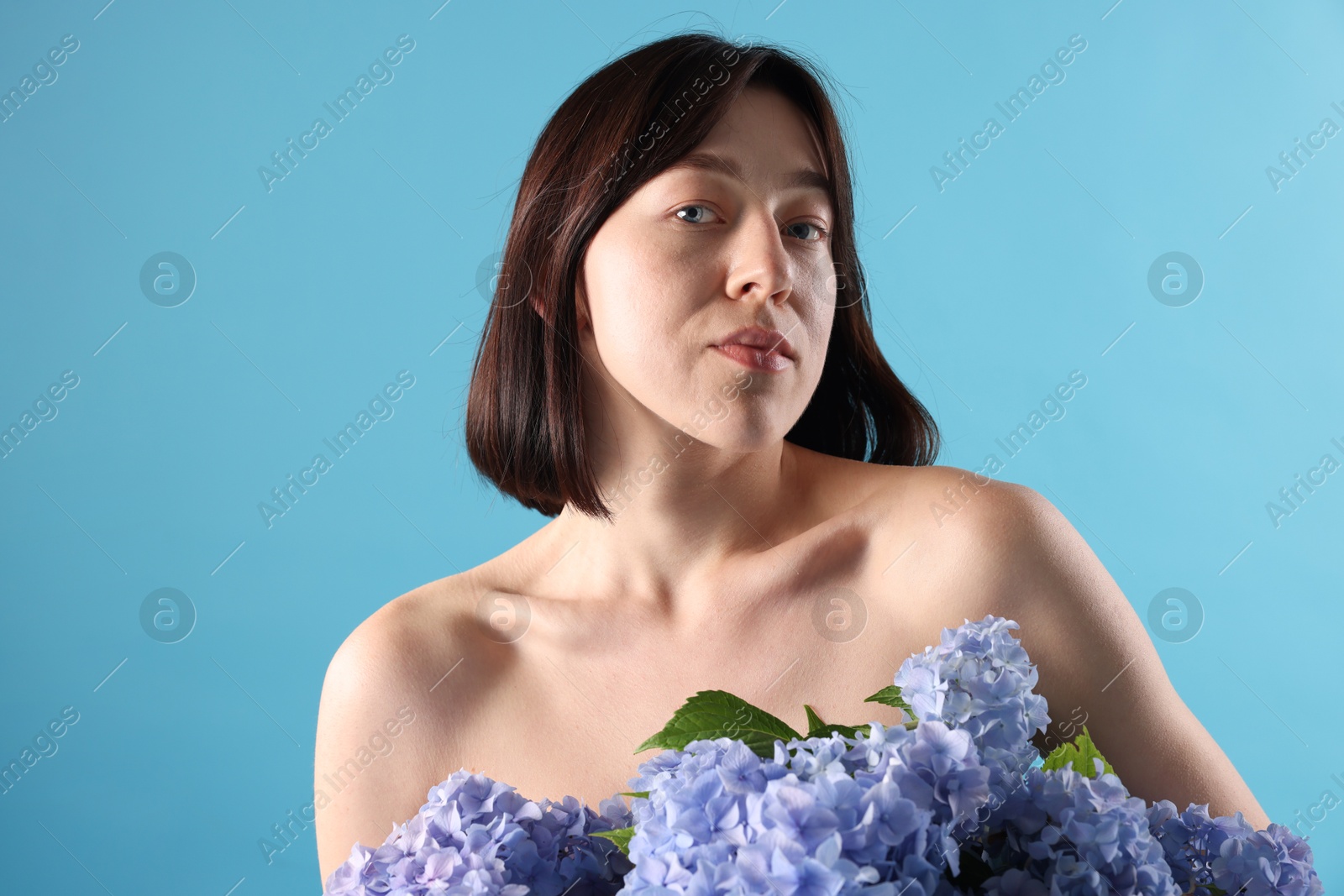 Photo of Beautiful young woman with hortensia flowers on light blue background