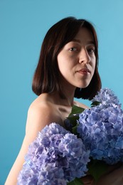 Photo of Beautiful young woman with hortensia flowers on light blue background