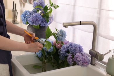 Photo of Woman pruning hortensia flowers with shears over kitchen sink, closeup