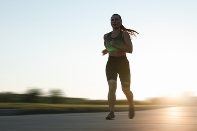 Image of Woman in sportswear running outdoors on sunny morning, motion blur effect. Low angle view