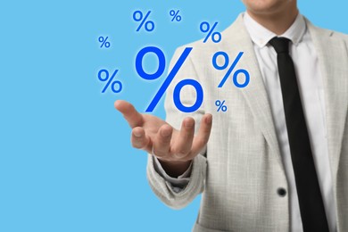 Image of Businessman holding virtual percent signs against light blue background, closeup
