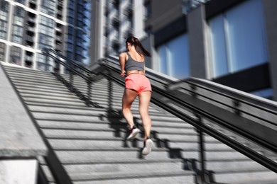 Image of Woman in sportswear running up on stairs outdoors, motion blue effect. Low angle view