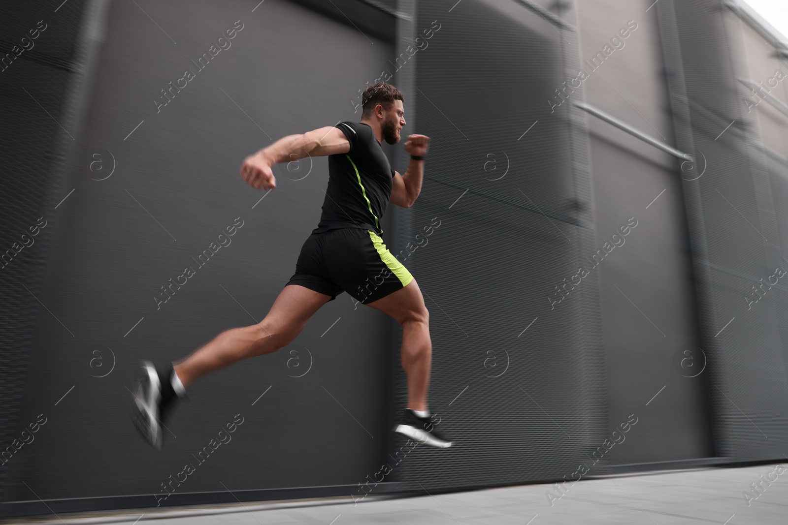 Man in sportswear running near building outdoors, motion blur effect. Low angle view Image of Man in sportswear running near building outdoors, motion blur effect. Low angle view