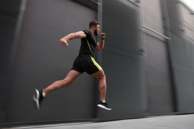 Image of Man in sportswear running near building outdoors, motion blur effect. Low angle view